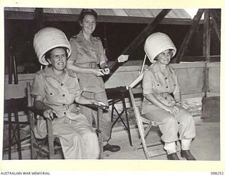 LAE, NEW GUINEA. 1945-10-10. LIEUTENANT S.H. BUDGE, AMENITIES OFFICER, AUSTRALIAN WOMEN'S ARMY SERVICE BARRACKS (1) AND MISS BURCHMORE, YWCA REPRESENTATIVE (3), USING HAIR DRYERS CONSTRUCTED BY LAE ..