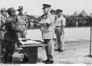 Lieutenant General Hatazo Adachi, GOC XV111 Japanese Army, surrendering his sword to Major General H C H Robertson, GOC 6th Australian Division, before 3,000 troops of the 6th Division during the ..