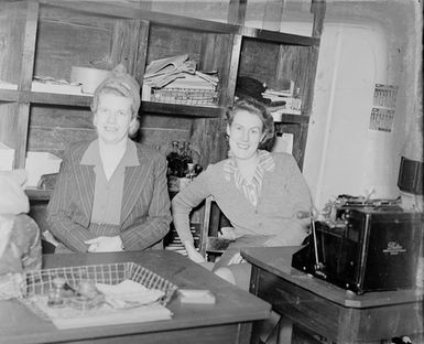 [Portrait of two women seated in front of tables or desks]