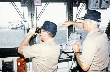 RADM William Retz, commander, Naval Base, Pearl Harbor, and CAPT Douglas Bradt, commanding officer of the amphibious assault ship USS BELLEAU WOOD (LHA-3), watch from the ship's bridge as supplies are unloaded from the vessel by members of Joint Task Force Garden Isle. The task force was organized to provide disaster relief for residents of the area in the aftermath of Hurricane Iniki