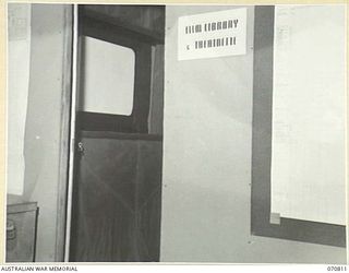 PORT MORESBY, NEW GUINEA, 1944-03-08. THE THEATRETTE AT "G" (VISUAL TRAINING), HEADQUARTERS, NEW GUINEA FORCE, VIEWED FROM THE OFFICE. ON THE RIGHT OF THE DOORWAY CAN BE SEEN ONE OF THE 16MM FILM ..