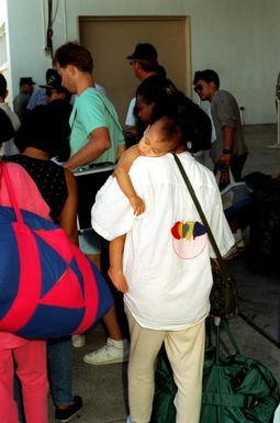 A mother carries her sleeping child as she and other evacuees from bases in the Philippines congregate in the base gym while stopping over en route to the United States. Civilian and military personnel and their dependents have been evacuated from Naval Station, Subic Bay and Naval Air Station, Cubi Point as part of Operation Fiery Vigil in the aftermath of Mount Pinatubo's eruption on June 10th.