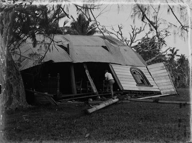 [Man inspecting damaged building with corrugated iron roofing]