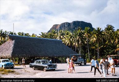 Tahiti - building and car park with people, mountain in distance