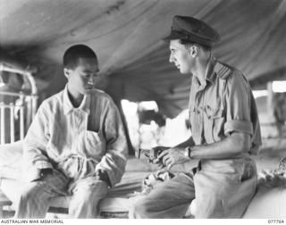 LAE, NEW GUINEA. 1944-12-30. SENIOR REPRESENTATIVE WYSHAM, AUSTRALIAN RED CROSS SOCIETY ISSUING COMFORTS TO LIEUTENANT HOROSHI, MEDICAL OFFICER, JAPANESE ARMY WHO IS A PRISONER OF WAR AT THE 2/7TH ..