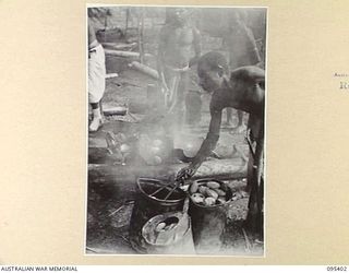 KIARIVU, NEW GUINEA, 1945-08-12. NATIVE COOKS PREPARING WHEATMEAL CAKES FRIED IN MUTTON FAT FOR AUSTRALIAN NEW GUINEA ADMINISTRATIVE UNIT NATIVES WHO ARE WORKING ON THE BUILDING OF THE AUSTRALIAN ..