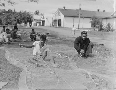 [A group of Pacific island men threading a fishing net]