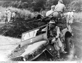 Munum Waters, Near Nadzab, New Guinea. 1943-09. Private Jack Johnson of Munda, Qld, relaxes while waiting for his jeep to be dragged out of the Yalu River