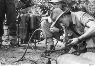 KARAWOP, NEW GUINEA. 1945-07-18. SERGEANT L.T. LEES, LAND HEADQUARTERS FLAME WARFARE TRAINING UNIT, CHARGING THE PRESSURE TANK OF A FLAMETHROWER DURING A COURSE ON THE WEAPON HELD AT 2/6 CAVALRY ..