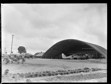 Bi-planes under a hangar with unidentified soldiers walking by, Nausori Airfield, Fiji